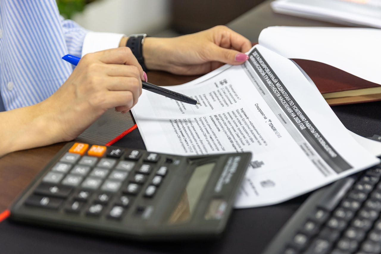 our-services-2 Close-up of a person analyzing financial documents using a calculator and pen.